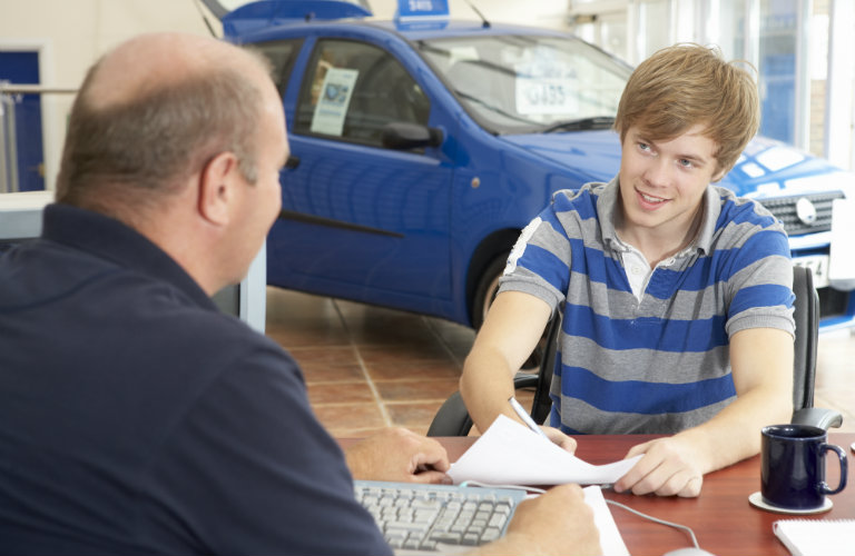Young-man-filling-out-paperwork-with-car-salesman