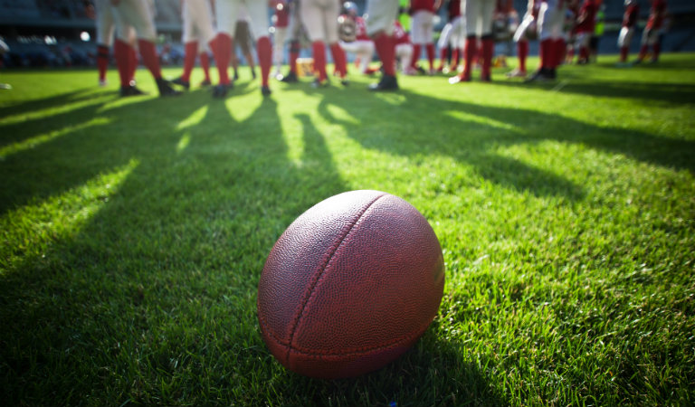 Football-laying-on-field-with-players-in-background
