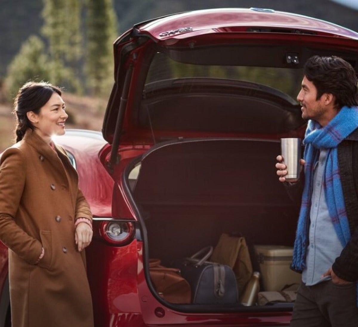 Two people standing near a Red Mazda CX-30 with the trunk open