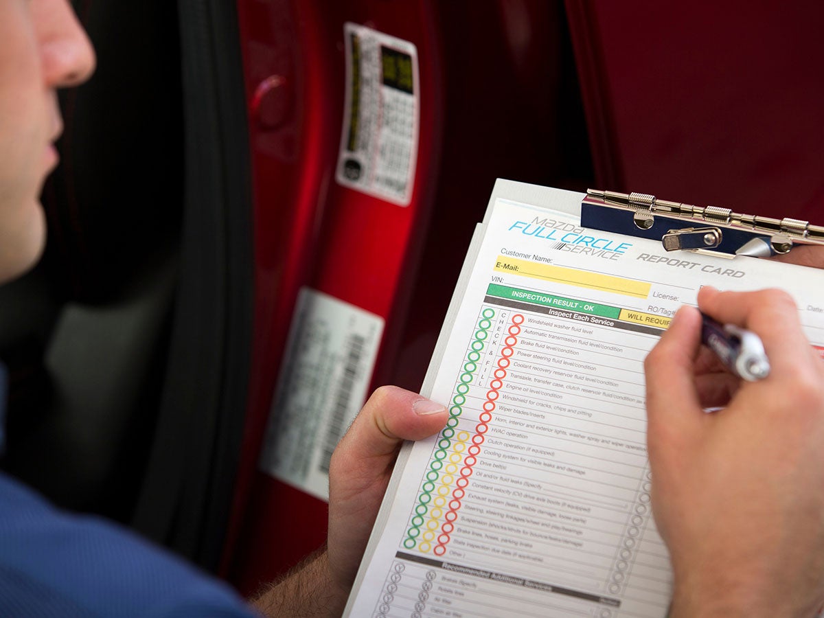 A Mazda technician servicing a vehicle using a checklist